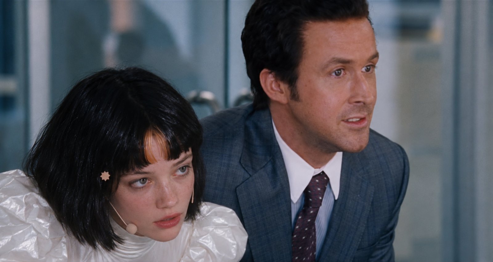 A film still of two people in an office, leaning forward to look at something off screen.